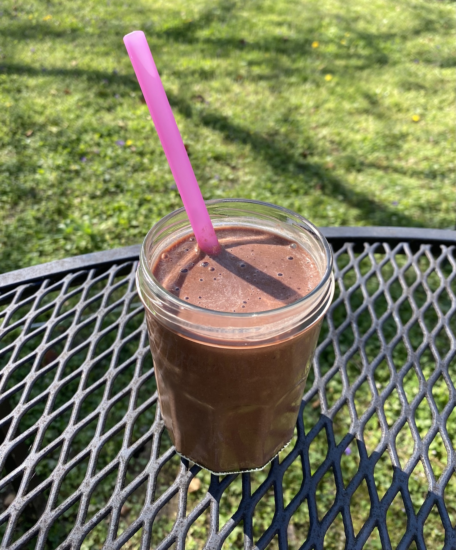 Chocolate banana oat smoothie in a clear glass on an outside table.