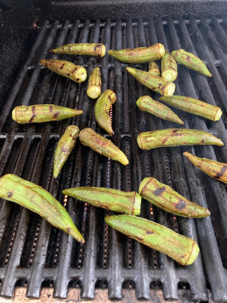 Okra pieces scattered on an outdoor grill top being cooked