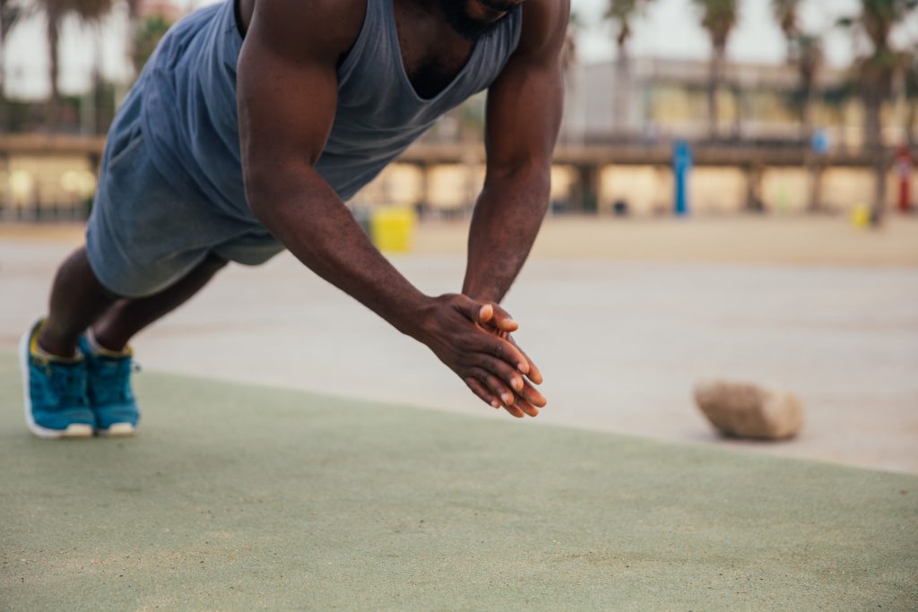 athletic black male performing a clapping push up mid-air with hands together.  