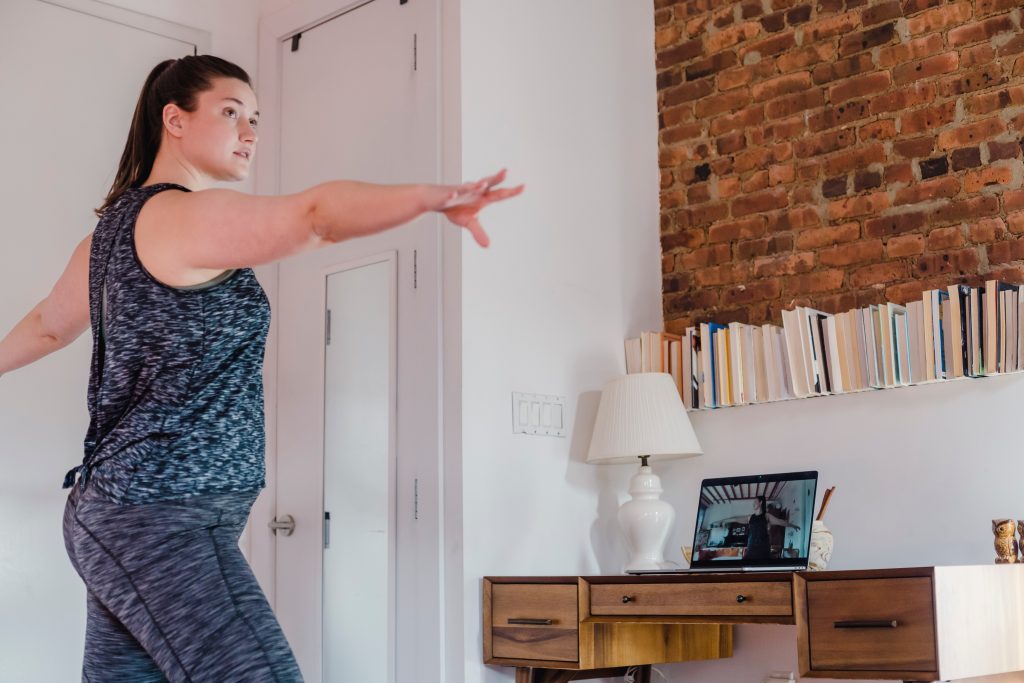 Women in athletic clothing working out in her bedroom using an online exercise class on a laptop