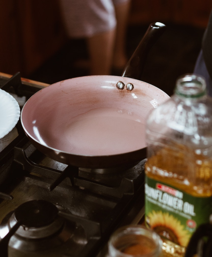 A plastic bottle of sunflower oil beside an empty pan on a gas stove