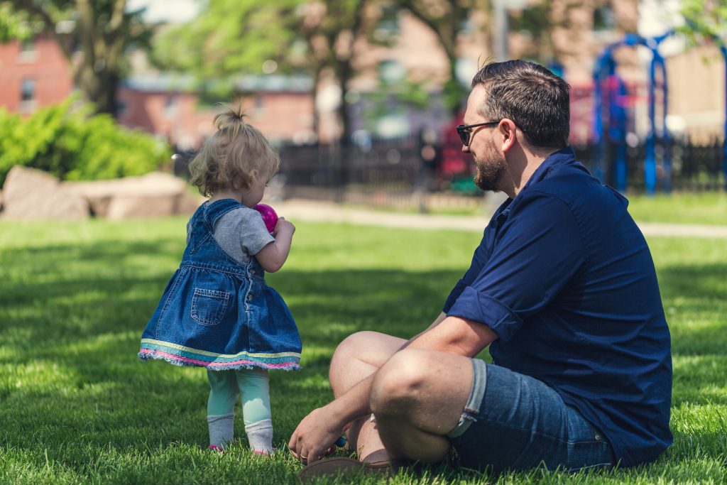 Dad sitting the grass and playing with his young daughter