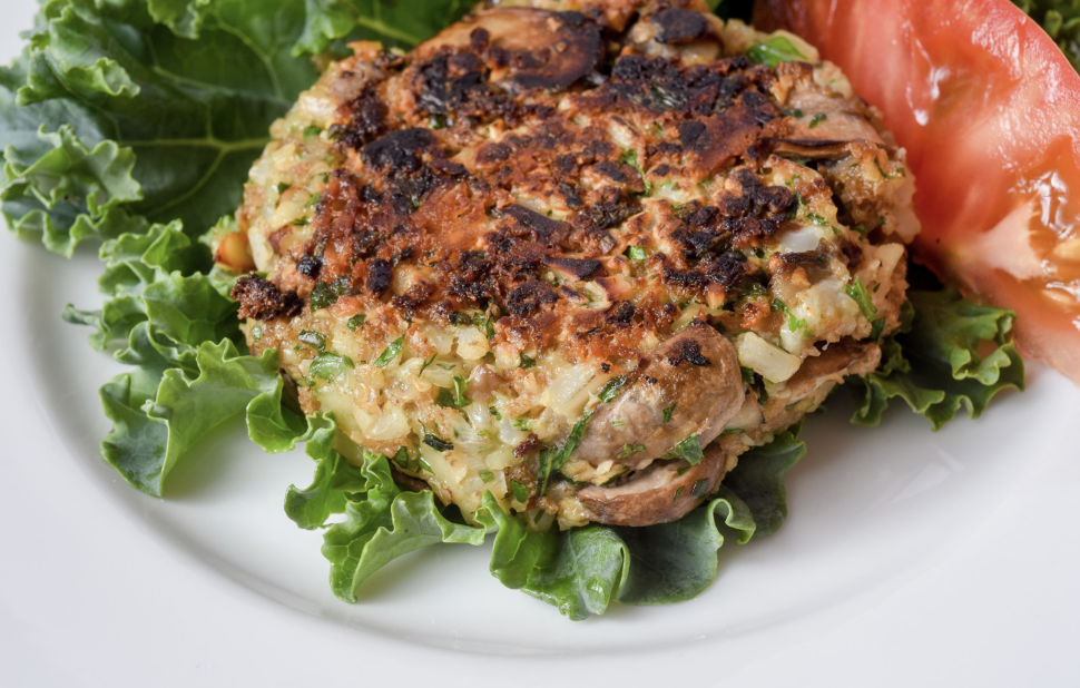 Mushroom almond burger served on a leaf of lettuce with a tomato wedge.
